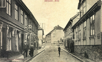 Storgata rundt 1905 ved krysset til Fleischers gate. Spinnhusgården / Brehmergården til venstre (brant i 1911). Postkortmotiv / fotograf ukjent